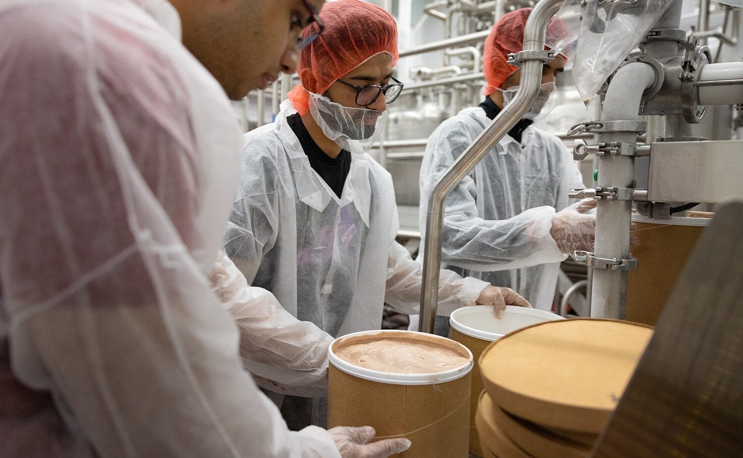 Three students add ice cream to three-gallon tubs in the Babcock Dairy Plant.